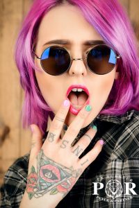 Close-up portrait of a modern girl with bright crimson hair and round sunglasses. Tattoo. Hair coloring. Optics style.